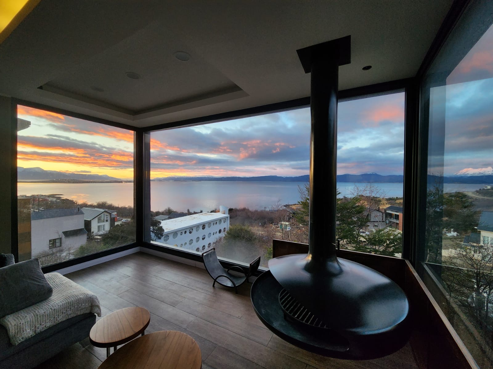 Sunset over the Beagle Channel seen from a Beagle Suites living room, with a suspended black fireplace beside floor to ceiling windows